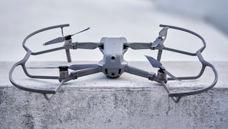 A sleek, modern drone sits on a concrete surface, equipped with a robust frame and four propellers. It appears to be designed for stability and efficiency, with aerodynamic features and a sturdy build. The drone's color seamlessly blends with its industrial setting.