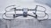 A sleek, modern drone sits on a concrete surface, equipped with a robust frame and four propellers. It appears to be designed for stability and efficiency, with aerodynamic features and a sturdy build. The drone's color seamlessly blends with its industrial setting.