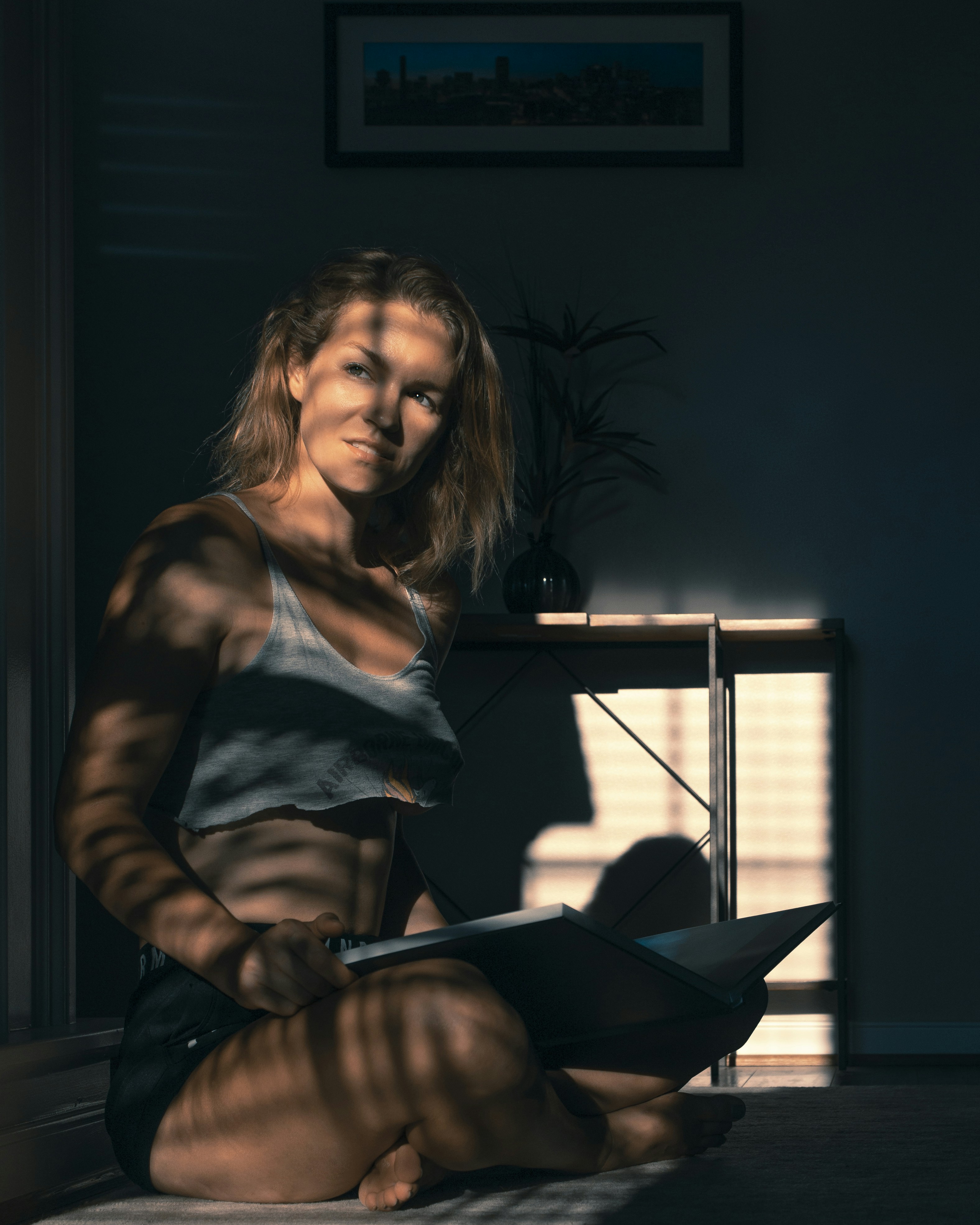 A woman working on a laptop in a studio, striped with window light