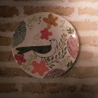A vibrant ceramic plate featuring a hand-painted bird design, catching the light beautifully.