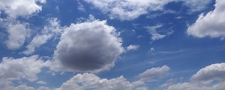 A vibrant sky with scattered white clouds against a backdrop of blue. The clouds vary in size and shape, with some appearing fluffy and others more wispy.