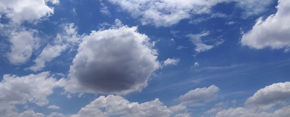 A vibrant sky with scattered white clouds against a backdrop of blue. The clouds vary in size and shape, with some appearing fluffy and others more wispy.