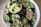 A vibrant assortment of fresh fruits arranged in a white bowl. Slices of kiwi, halved passion fruits, and clusters of green and purple grapes surround a hollowed pineapple filled with pineapple chunks and blueberries. Fresh mint leaves are scattered for added freshness.