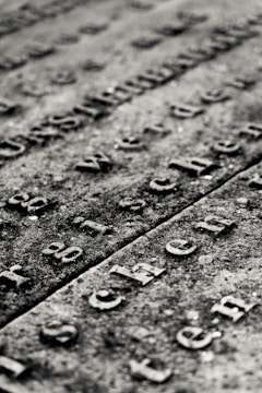 Weathered stone surface with engraved letters forming text. The lettering is old and slightly worn, with shadows accentuating the depth of the grooves.