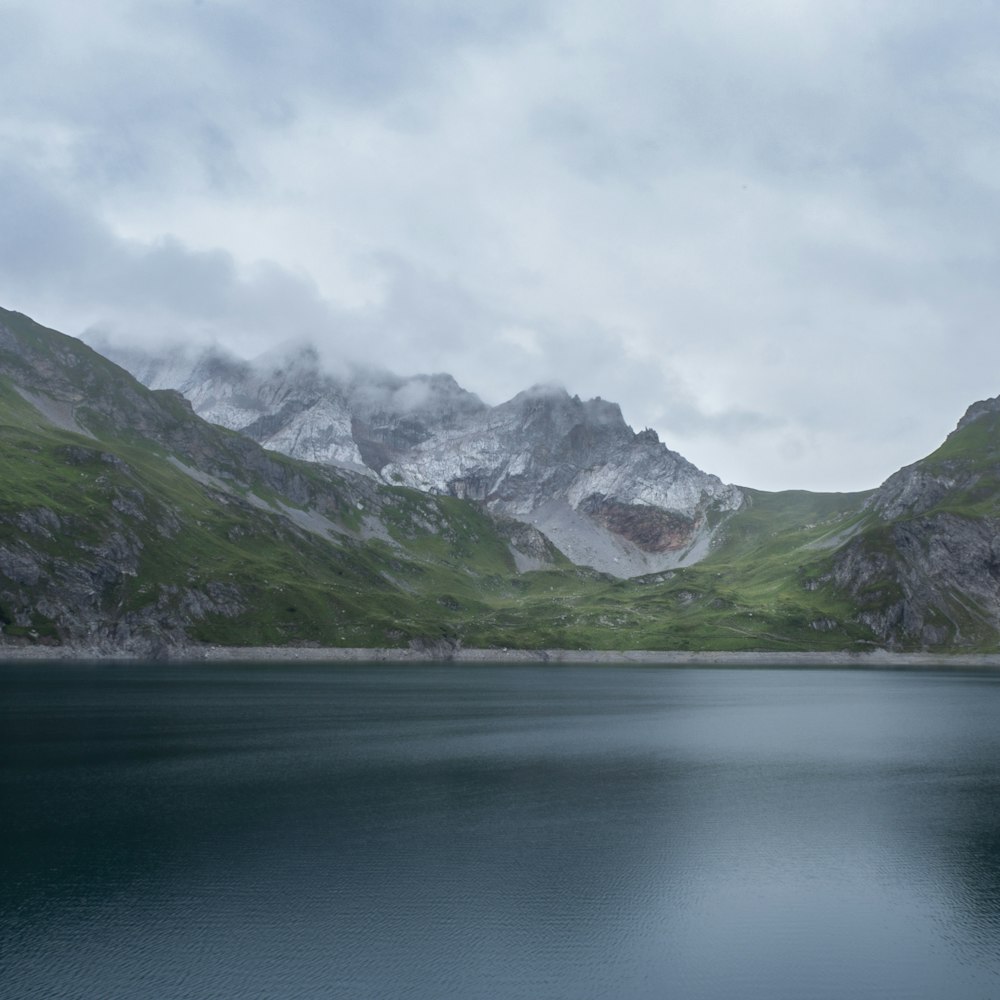 montañas verdes y blancas junto al cuerpo de agua bajo nubes blancas durante el día