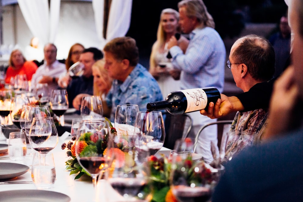 pessoas sentadas ao redor da mesa com taças de vinho e garrafa de vinho