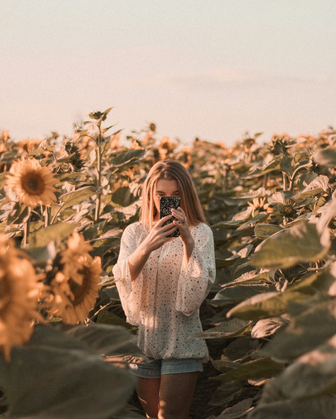 woman in white long sleeve dress standing on sunflower field during daytime