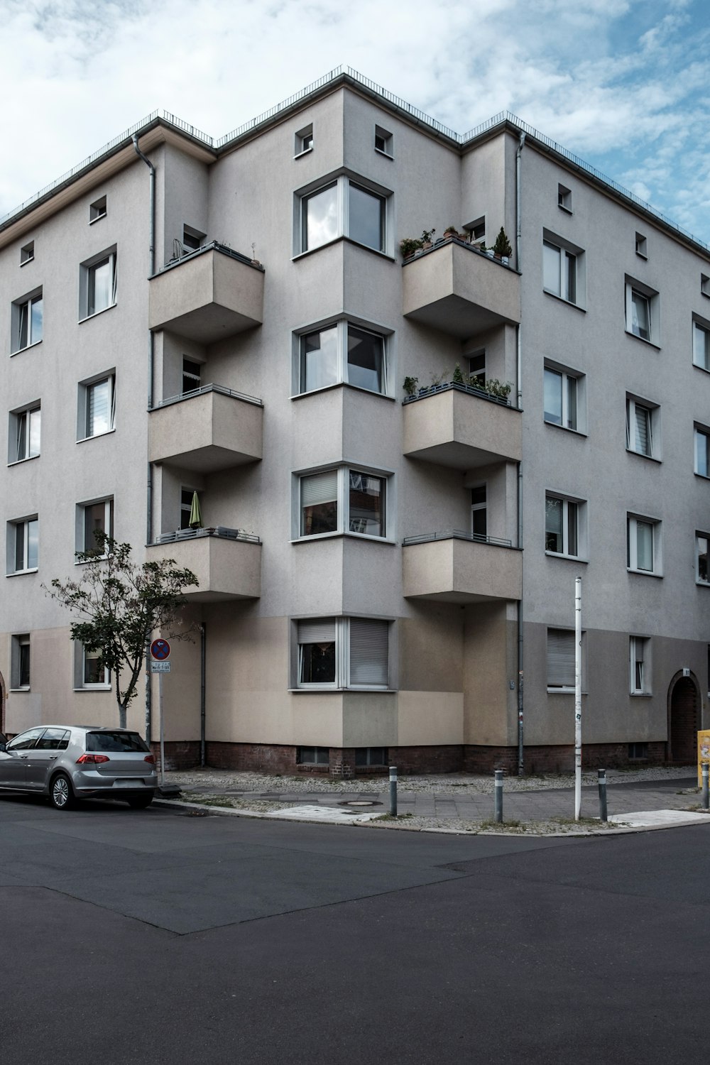 昼間は緑の木のそばに白いコンクリートの建物