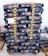 A stack of black bags labeled 'Cibau Adult 15kg', organized in a uniform manner on wooden pallets. The bags are secured with yellow and black caution tape. There is a small handwritten note placed on the stack and additional bags are visible at the side.