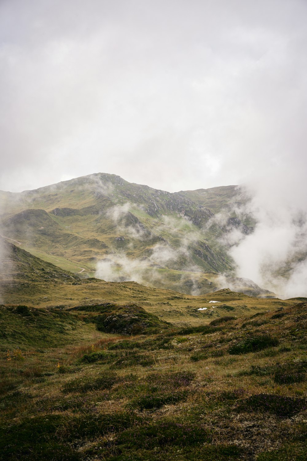 green grass field near mountain under white clouds during daytime