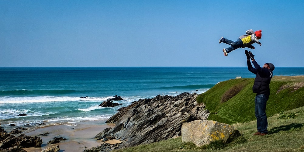 man jumping on rocky shore during daytime