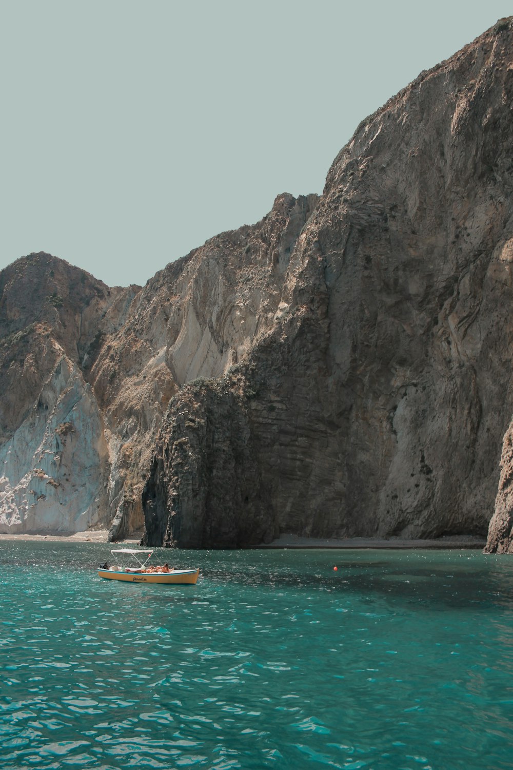 brown boat on sea near rocky mountain during daytime