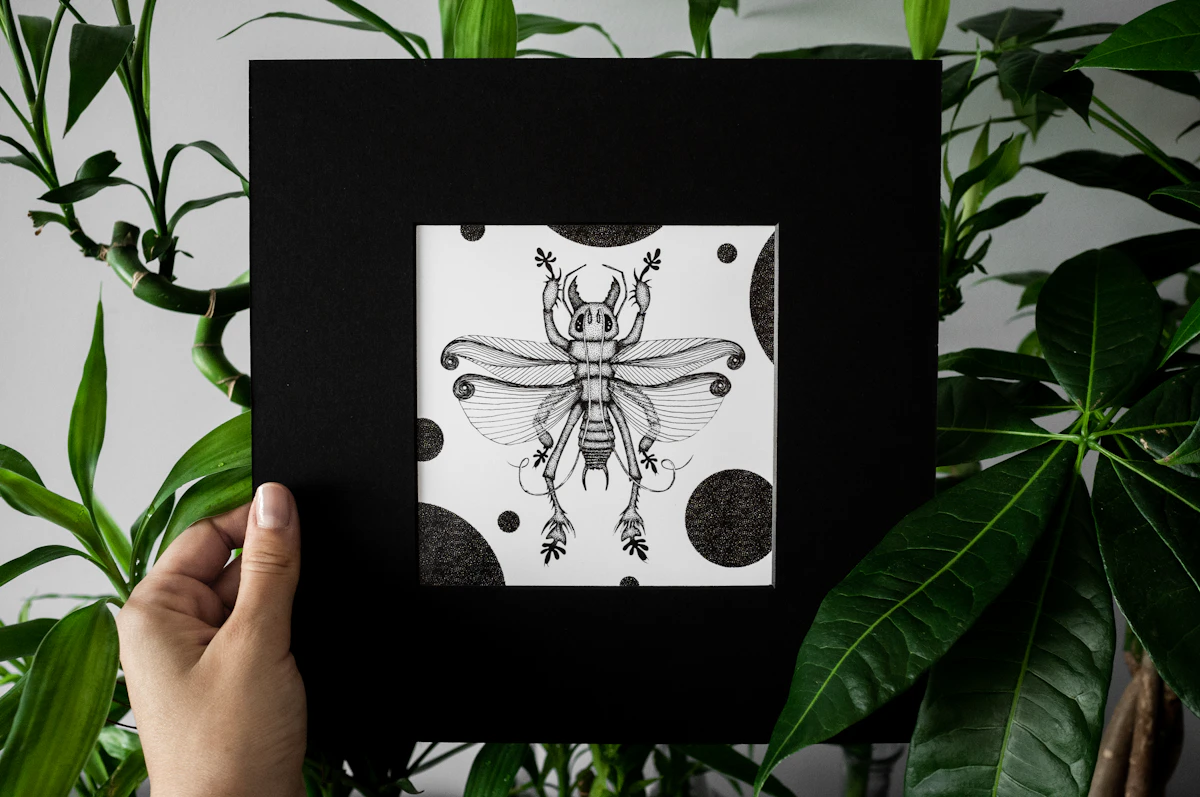 Hand holding a framed illustrated art print among plants