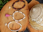 Stack of handmade pearl and bead bracelets in soft blush and gold tones, arranged on a wooden surface.