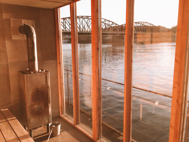 Warmly lit cozy riverside room with wooden furniture and a window showing flowing river.