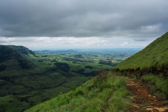 Expansive green land with rolling hills and a dirt path.