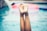 Legs are raised vertically out of the water in a swimming pool, with droplets of water visible on the skin. In the background, there's an out-of-focus inflatable pool ring.