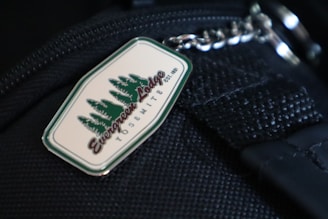 A metal keychain attached to a black fabric surface, featuring the logo 'Evergreen Lodge Yosemite' with an image of evergreen trees.