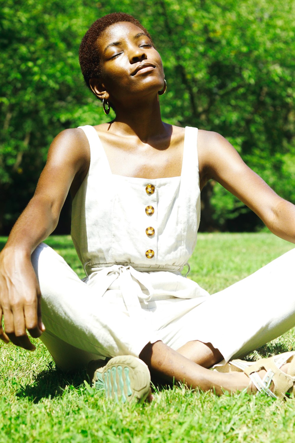 woman in white tank top and white pants sitting on white textile on green grass field
