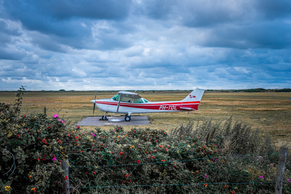 white and red airplane on brown field under white clouds during daytime