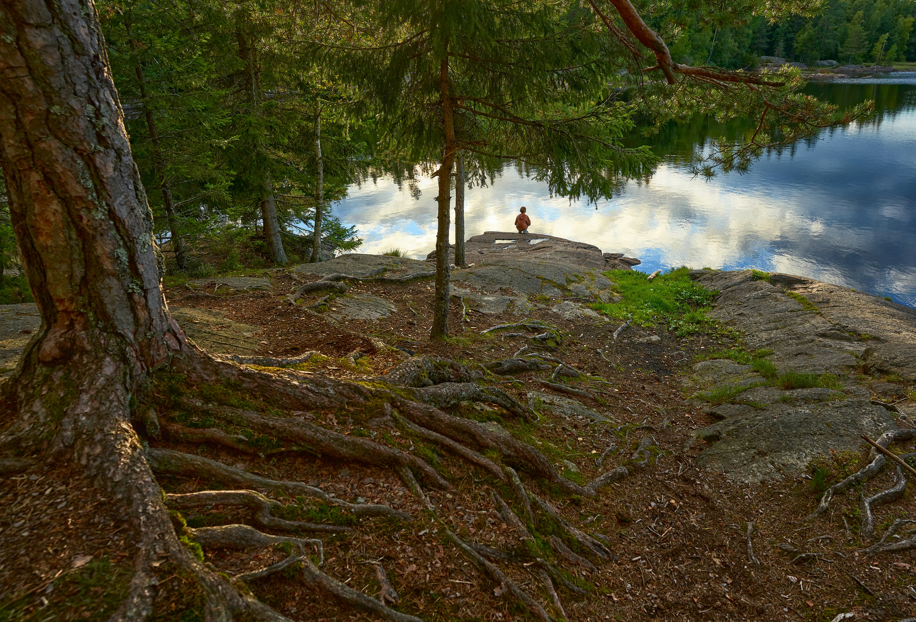 Persona con camisa blanca sentada en una roca cerca del cuerpo de agua durante el día