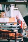 man in orange polo shirt standing in front of table