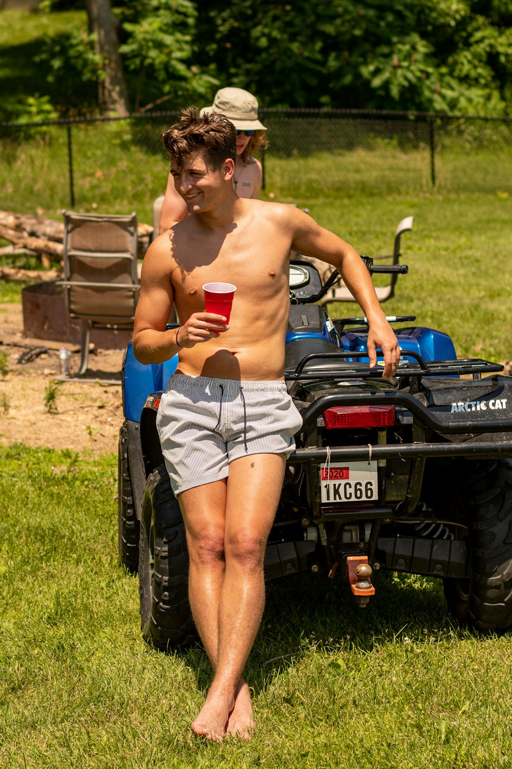 topless man in blue denim shorts standing beside black car during daytime