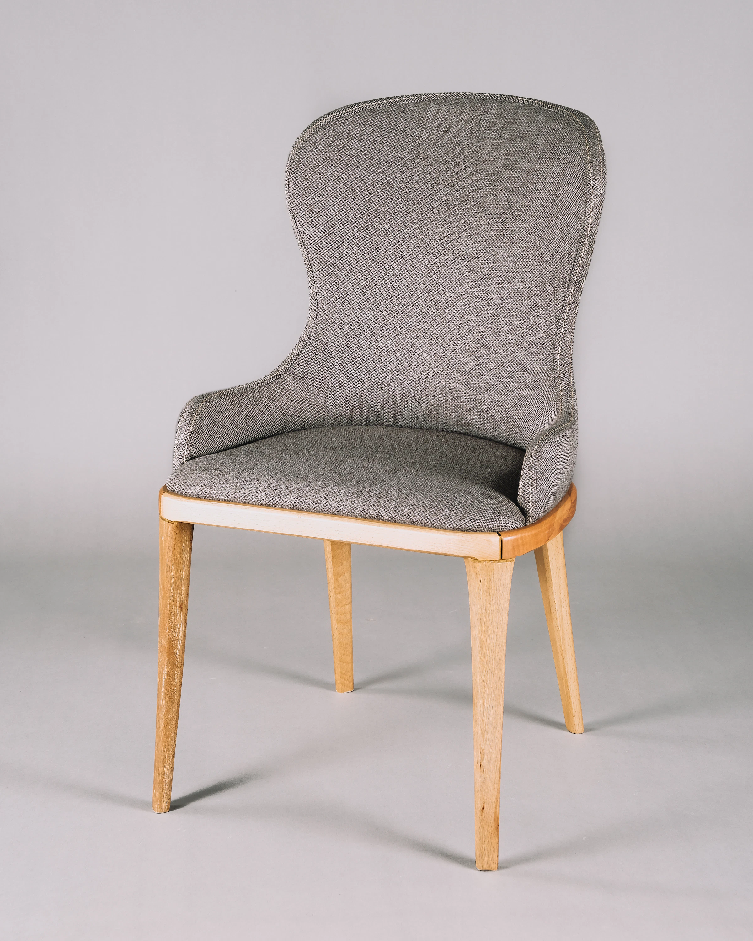 Studio photo of a modern grey upholstered chair with a high back and light wooden tapered legs