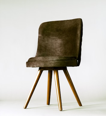 A modern chair with a cushioned backrest and seat in dark brown fabric. It features four wooden legs that taper slightly toward the ends, giving it a sleek and contemporary appearance. The chair is positioned against a plain, light-colored background.