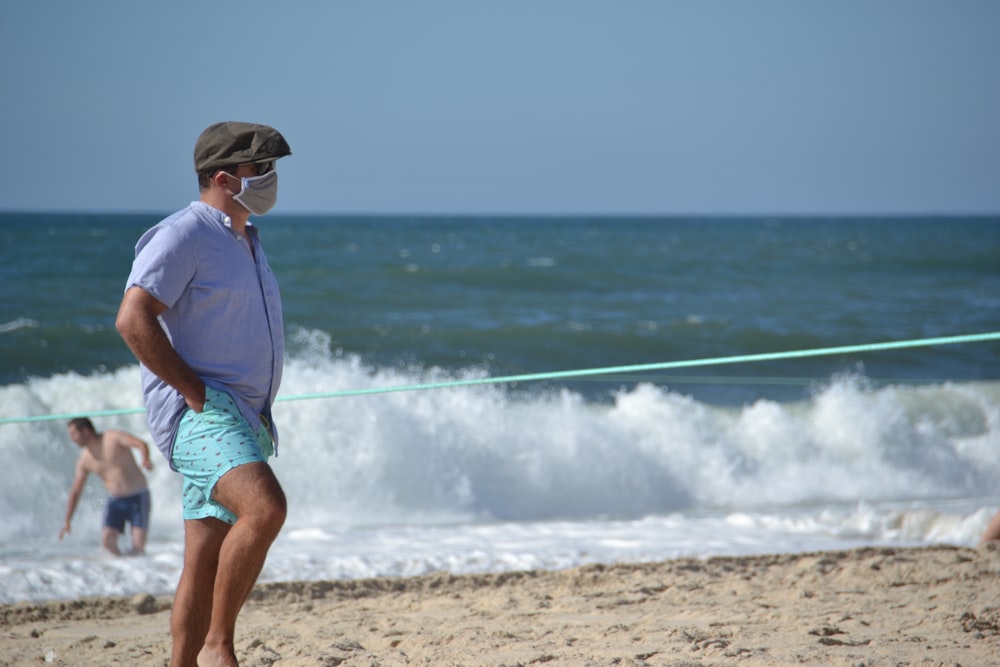 man in blue shirt and green shorts standing on beach shore during daytime
