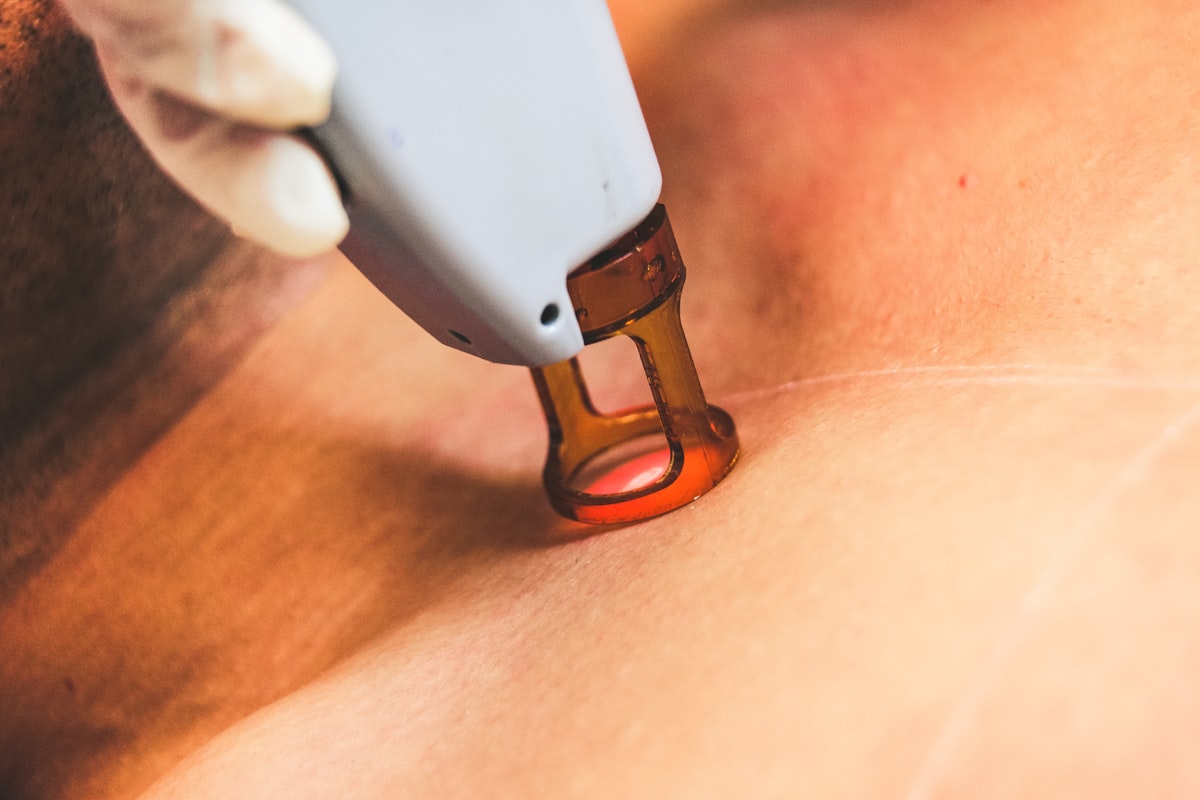 A hand holding a white and orange handheld treatment device
