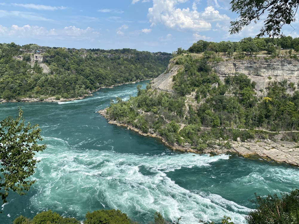 green water near brown rocky mountain under blue and white sunny cloudy sky during daytime