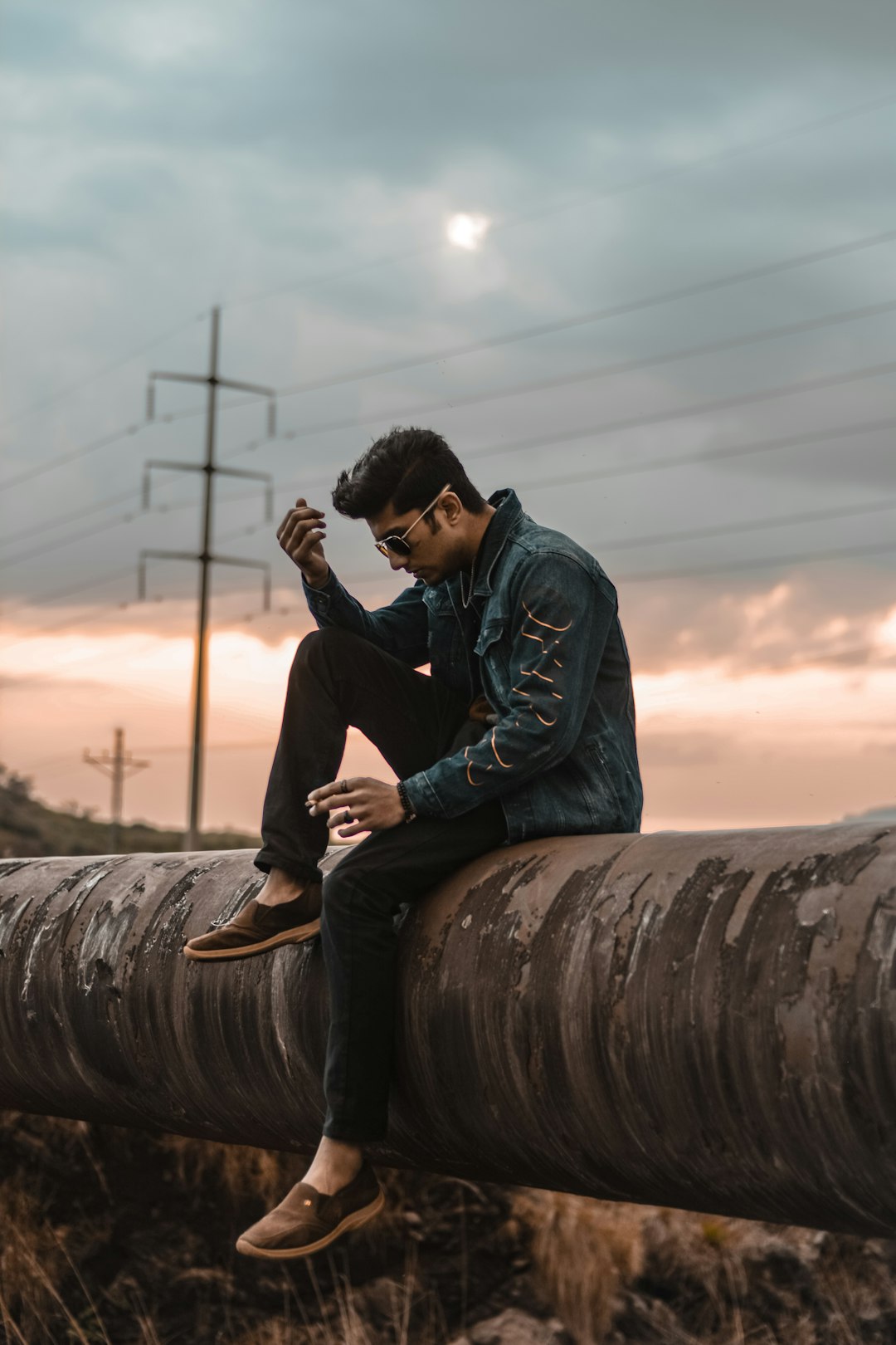 man in black jacket sitting on brown wooden post during sunset