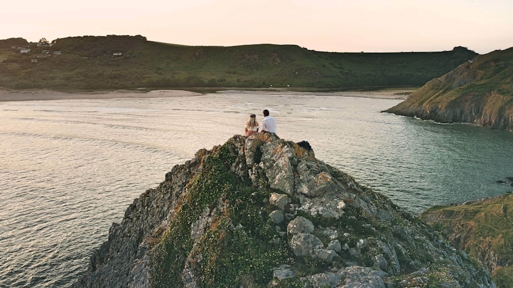 person in white shirt sitting on rock near body of water during daytime