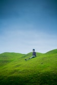A person pausing on a hilltop, breathing deeply while overlooking rolling green fields.