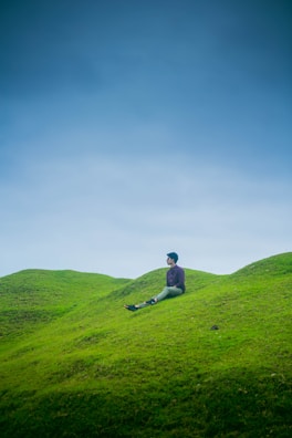 A person pausing on a hilltop, breathing deeply while overlooking rolling green fields.