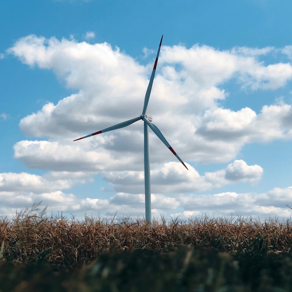 wind turbine on brown grass field under blue and white cloudy sky during daytime