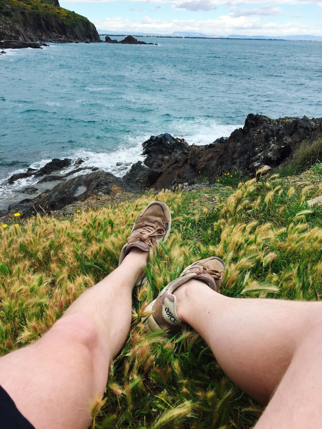 person wearing brown leather sandals sitting on rock near body of water during daytime