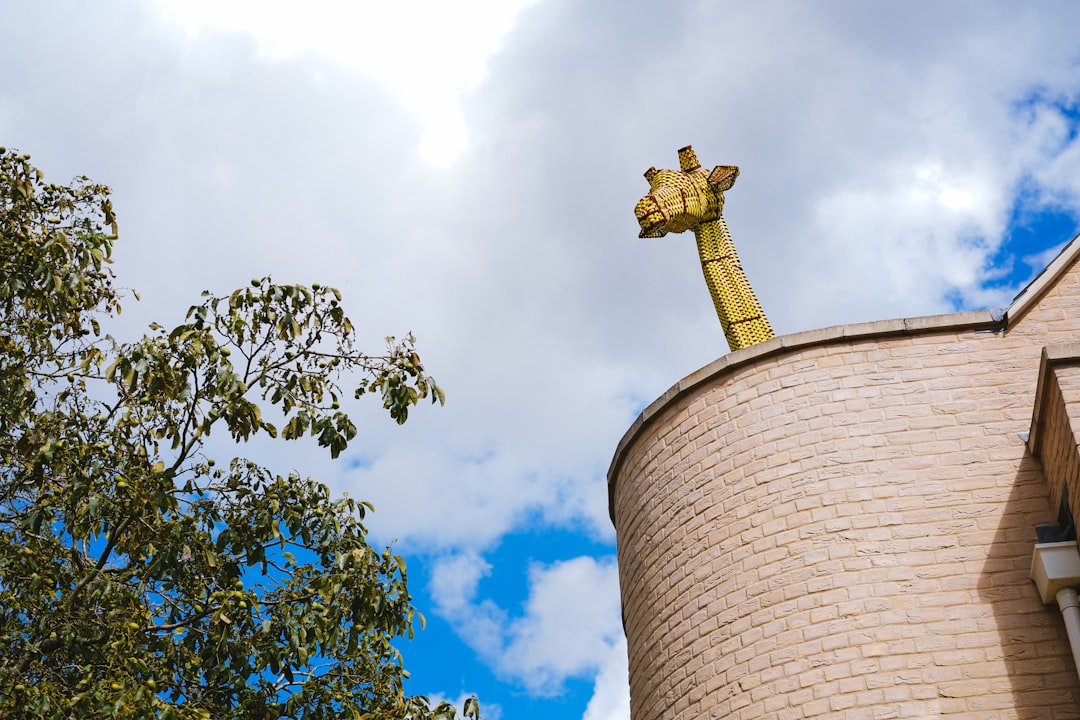 brown cross on brown concrete tower under white clouds and blue sky during daytime