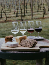 A rustic wooden board displaying an assortment of cheeses, cured meats, nuts, and fresh bread, set beside a glass of red wine at the winery.
