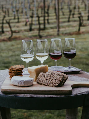 A rustic wooden board displaying an assortment of cheeses, cured meats, nuts, and fresh bread, set beside a glass of red wine at the winery.