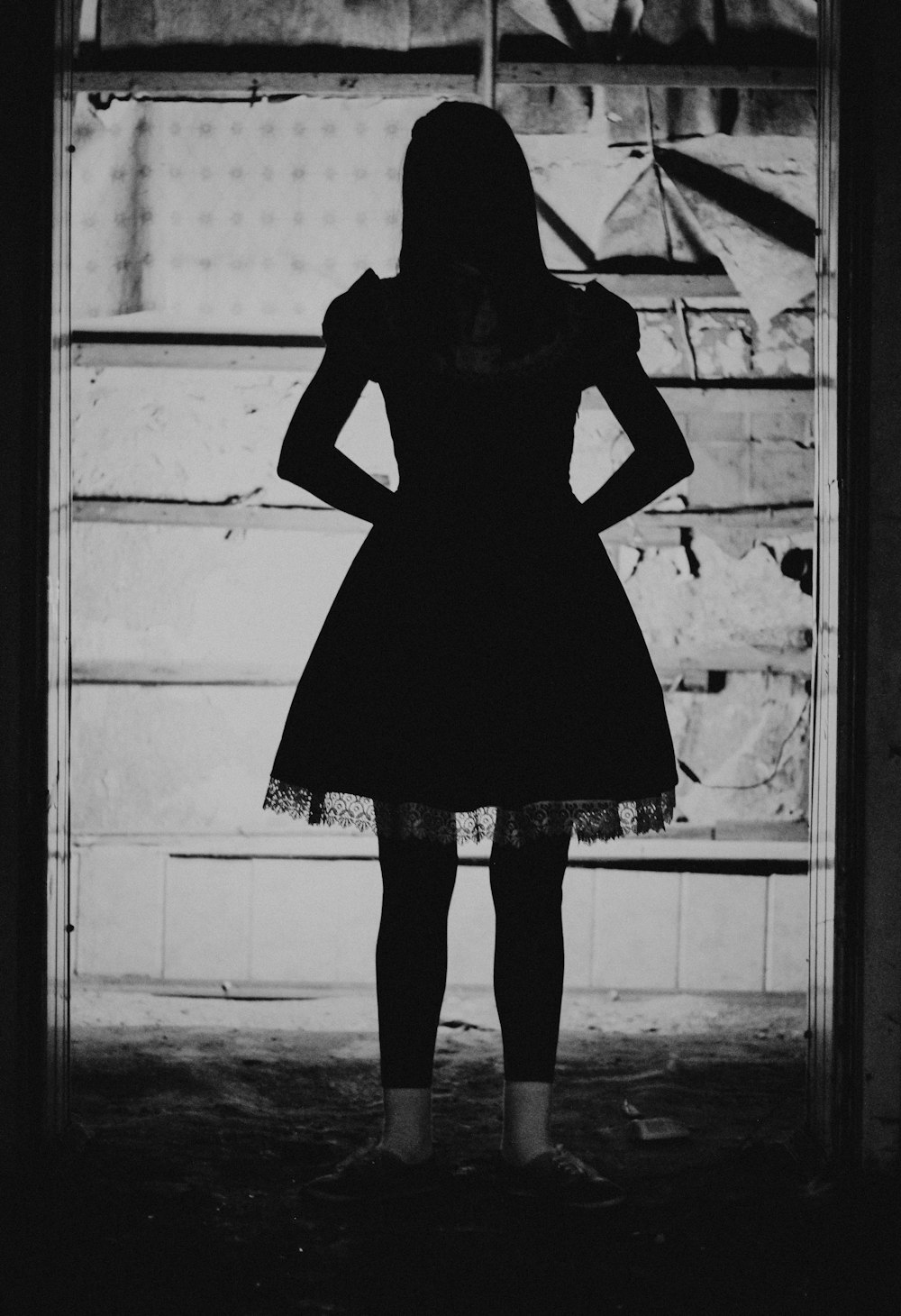 una donna in piedi davanti a una finestra con le mani sui fianchi