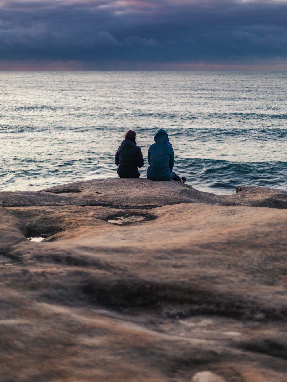 man in black jacket sitting on brown rock near sea during daytime