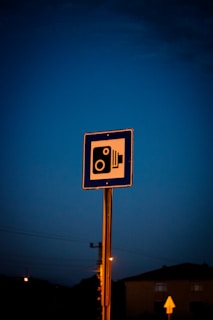 A close-up of a license plate reader camera mounted on a streetlight against a dusky city skyline.