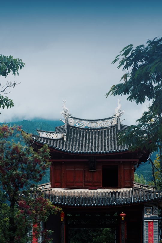 brown and black temple surrounded by green trees under white sky during daytime in Dali China