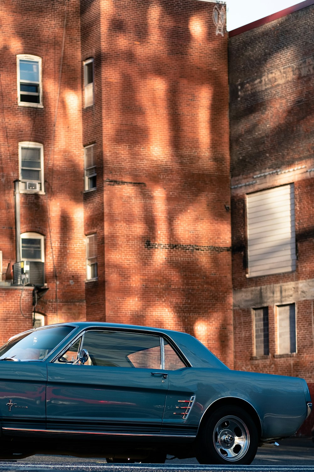 日中、茶色のレンガ造りの建物の脇に駐車された青いクーペ