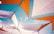 Geometric shapes are formed by interconnected white and orange fabric panels, set against a clear blue sky. The panels are structured with black netting and borders, creating an abstract and artistic canopy.