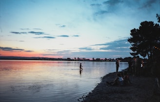 A serene lakeside view at sunset with a small group gathered in a circle for a healing session during the mental health conference retreat.