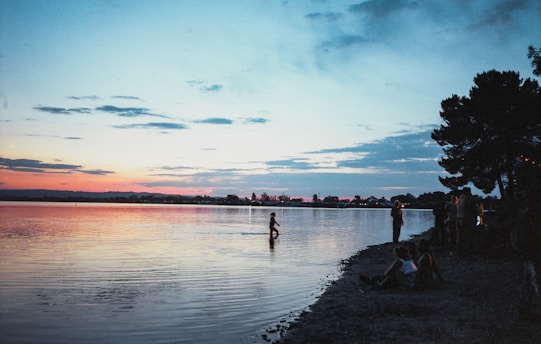 A serene lakeside view at sunset with a small group gathered in a circle for a healing session during the mental health conference retreat.
