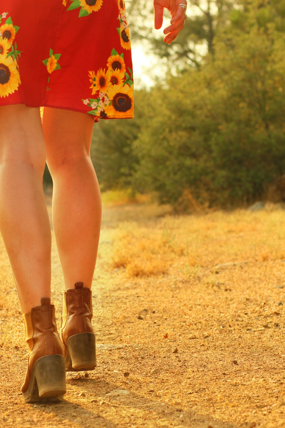 woman in red floral dress and brown leather boots standing on brown grass field during daytime